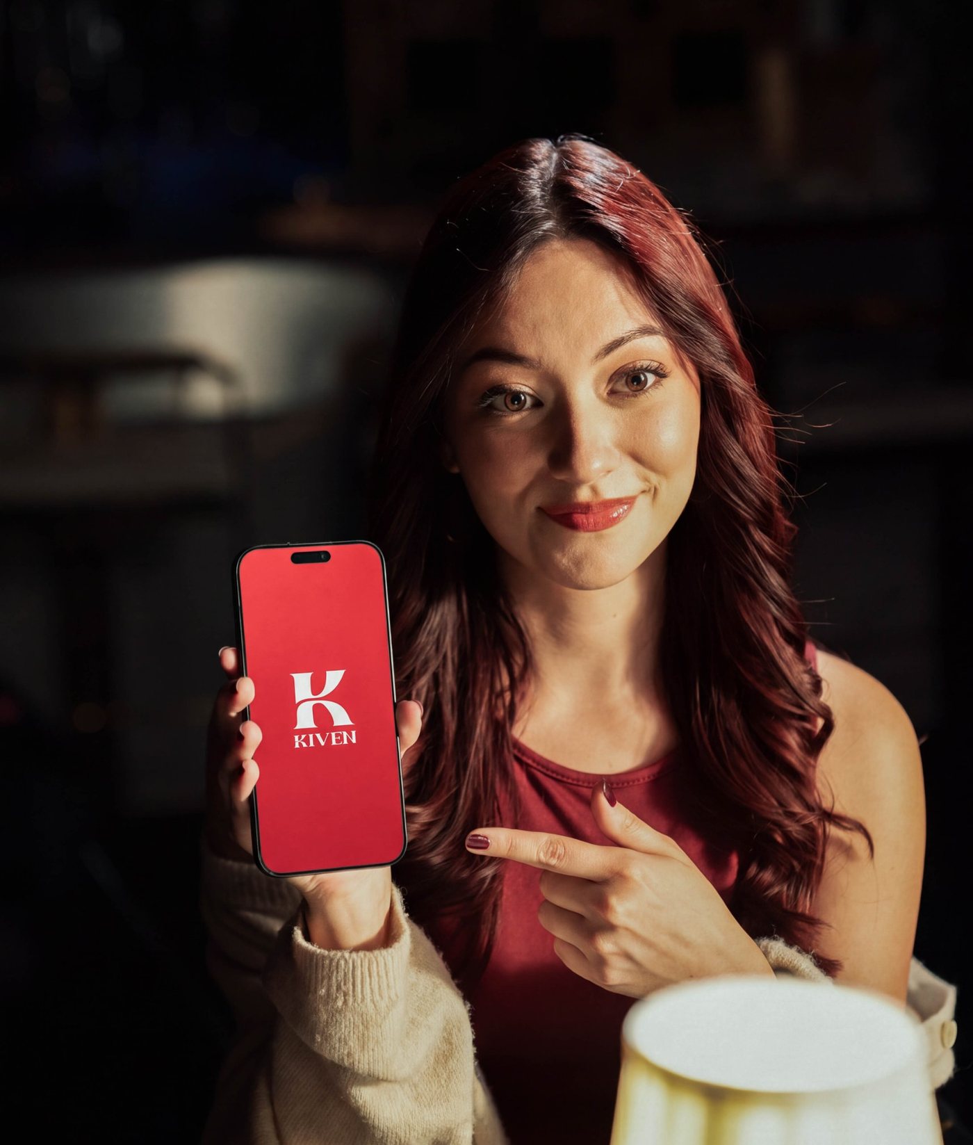A woman at a restaurant table pointing at the Kiven app on her phone