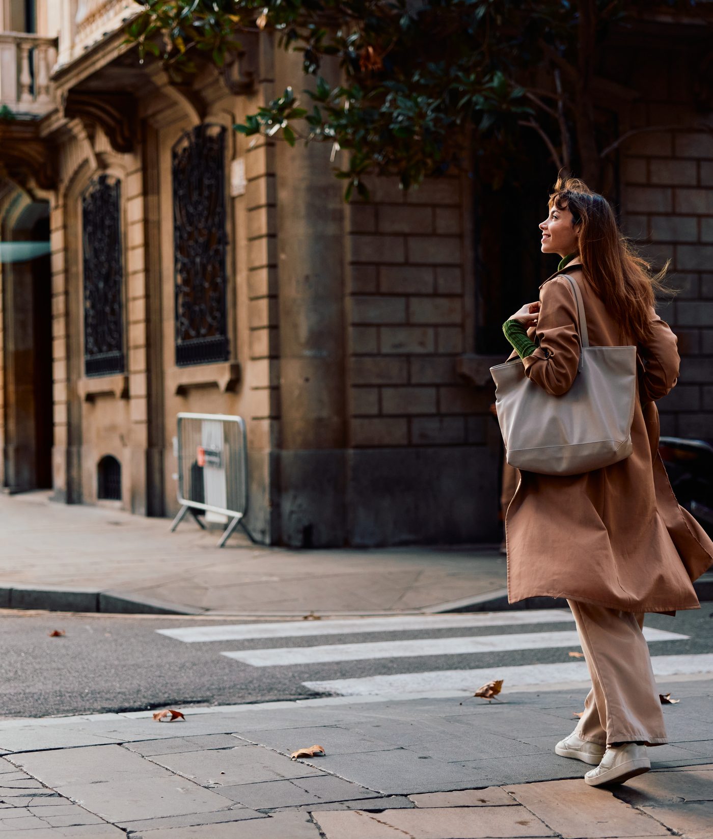 A woman in a camel coat walking through a sunlit city street