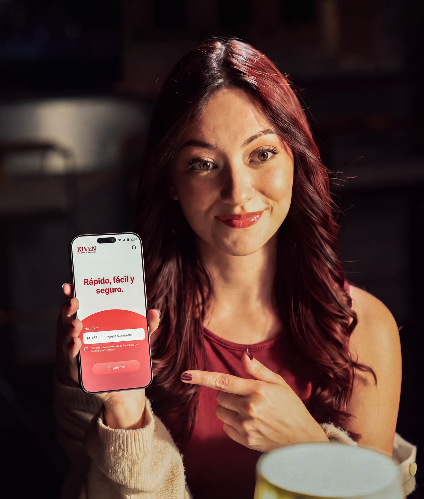 A woman at a restaurant table pointing at the Kiven app on her phone