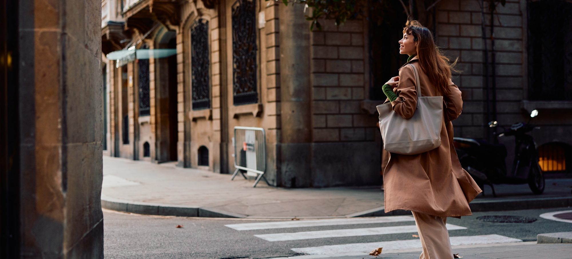 A woman in a camel coat crossing a sunlit city street