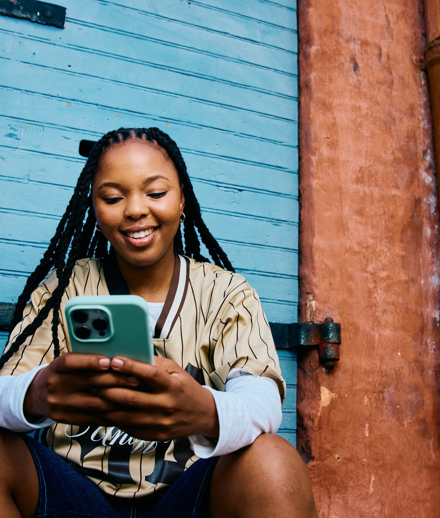 A woman smiling at her phone in front of a blue wooden door